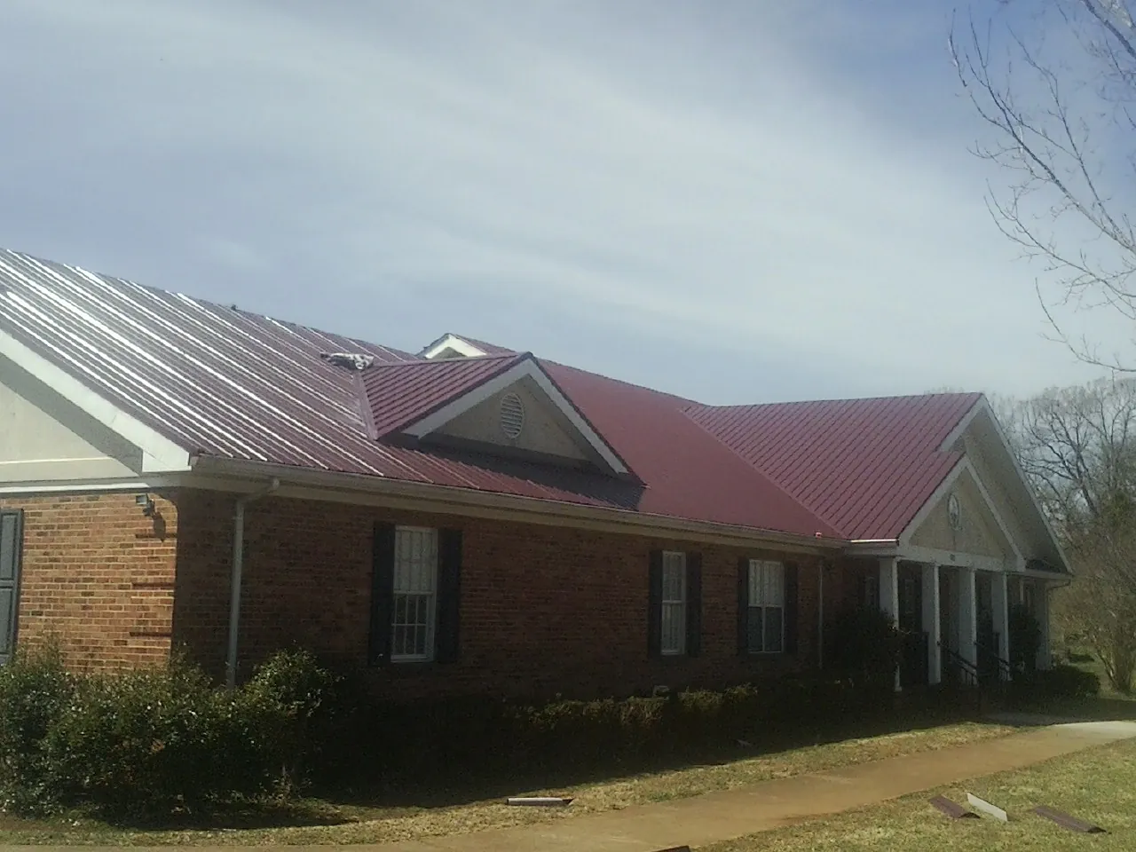 Red metal roof with gabled entries on a long brick building, from a Hail Damage Roof Repair job in Shirleysburg
