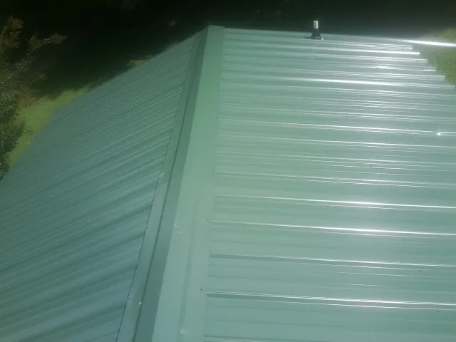 New green metal panels meeting at the ridge of a roof — Flat Roof Repair work by our crew in Shirleysburg