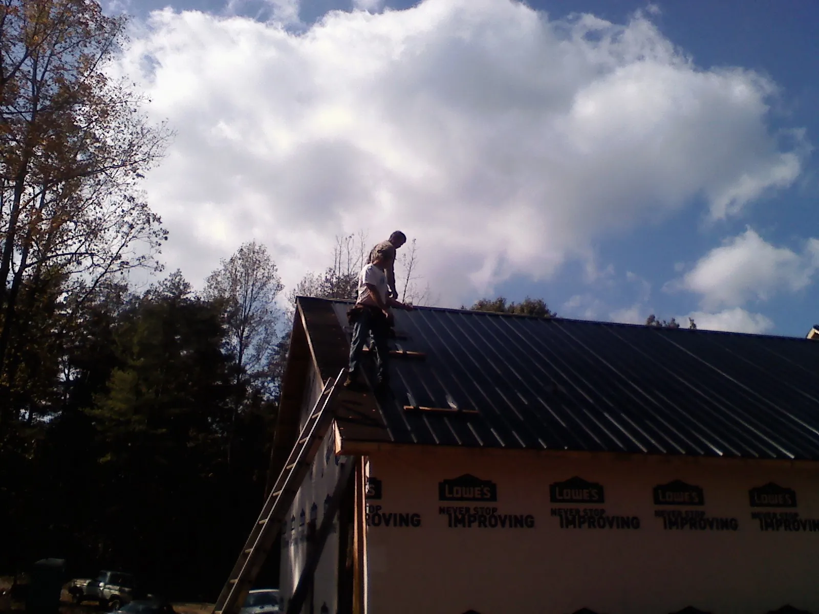 Roofer fastening dark metal panels high against a cloudy sky, from a Roof Inspection job in Shirleysburg