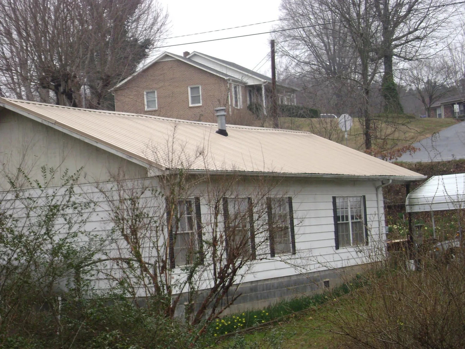 Tan metal roof on a white sided house set into a hillside — Commercial Roofing by Roofing Brothers in Shirleysburg